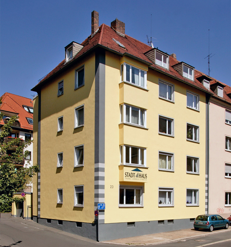 Viergeschossiges, gelbes Mehrfamilienhaus mit roten Dachziegeln und mehreren Dachgauben, Standort an der Franz-Ludwig-Straße in Würzburg.