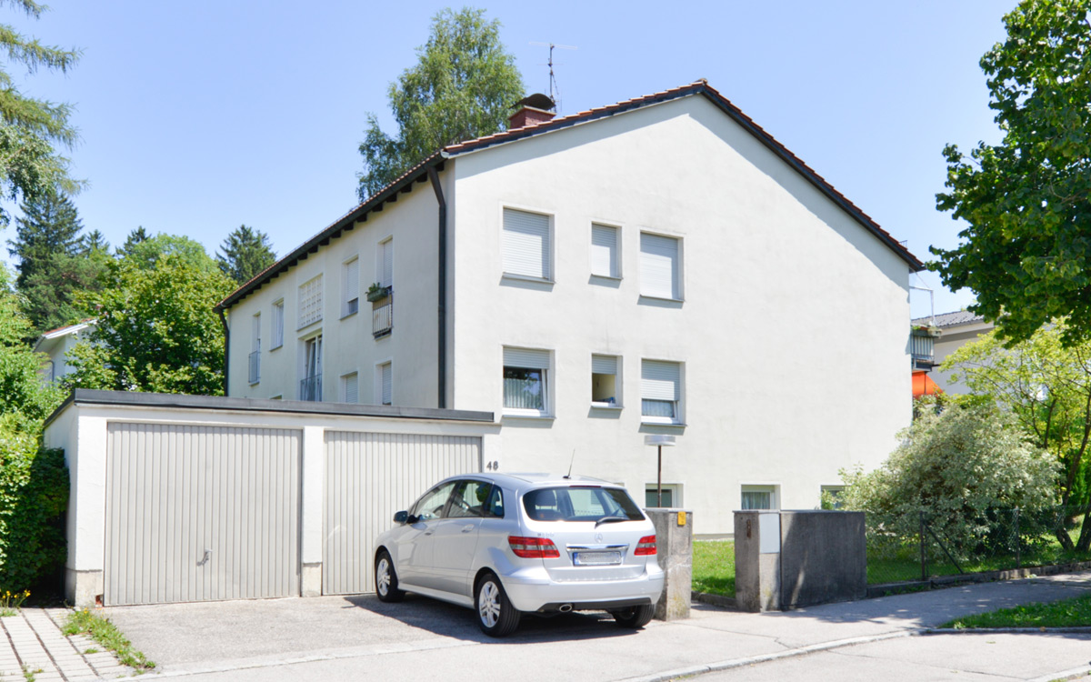 Zweigeschossiges weißes Wohngebäude mit Satteldach, rechteckigen Fenstern und angrenzender Garage, davor ein geparktes Auto; Standort Saalachstraße, Traunstein.