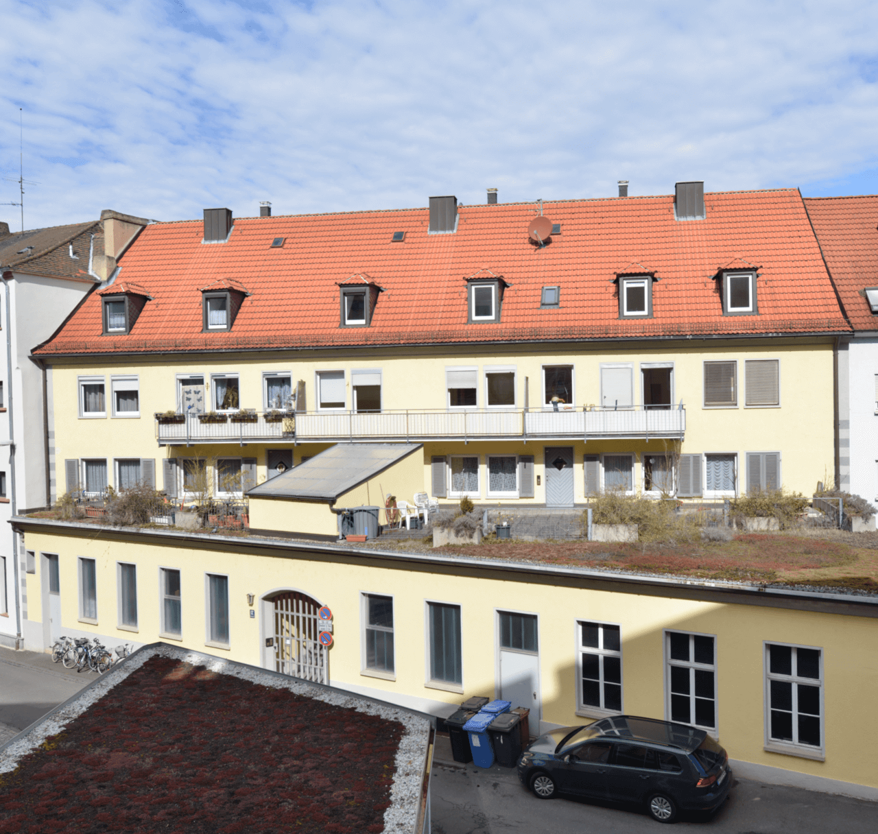 Zweigeschossiges Wohngebäude mit heller Fassade und ausgebautem Dachgeschoss, Balkonreihe im Obergeschoss, Zufahrt mit Pflasterfläche im Vordergrund.